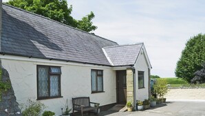 A white building with a dark roof, a stone wall, and a paved driveway. - Pant Glas Mawr Axton (Axton, near Holywell)