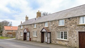 A stone building with multiple windows and doors, a paved driveway, and a red-roofed building in the background. - 3 bedroom accommodation in Dunstan, near Craster (Dunstan, near Craster)