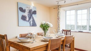 A dining area with a wooden table set for six, surrounded by six chairs. There is a painting of a cow on the wall above the table. - 3 bedroom accommodation in Dunstan, near Craster (Dunstan, near Craster)