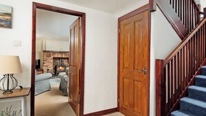 A wooden staircase with a carpeted landing, a wooden door, and a view into a living room with a fireplace. - 3 bedroom accommodation in Dunstan, near Craster (Dunstan, near Craster)