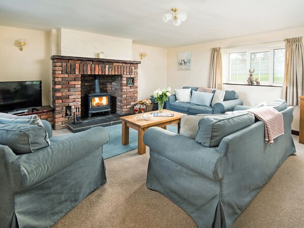 A cozy living room with a brick fireplace, a flat-screen TV, grey sofas, and a wooden coffee table. - 3 bedroom accommodation in Dunstan, near Craster (Dunstan, near Craster)