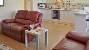 Una cocina moderna con estufa a gas, horno y microondas. Hay un rincón de comedor con un sofá de cuero marrón y una mesa pequeña con una botella de vino y copas.