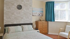 Un dormitorio con una cama, un aparador, una silla, un reloj y un cuadro en la pared.