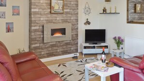 Una sala de estar con chimenea, televisor y sofás de cuero rojo.