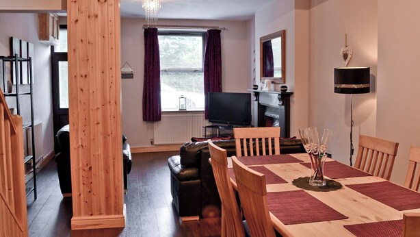 Ein gemütliches Wohnzimmer mit einem Holzesstisch, Stühlen, einem Fernseher und einem Kamin.