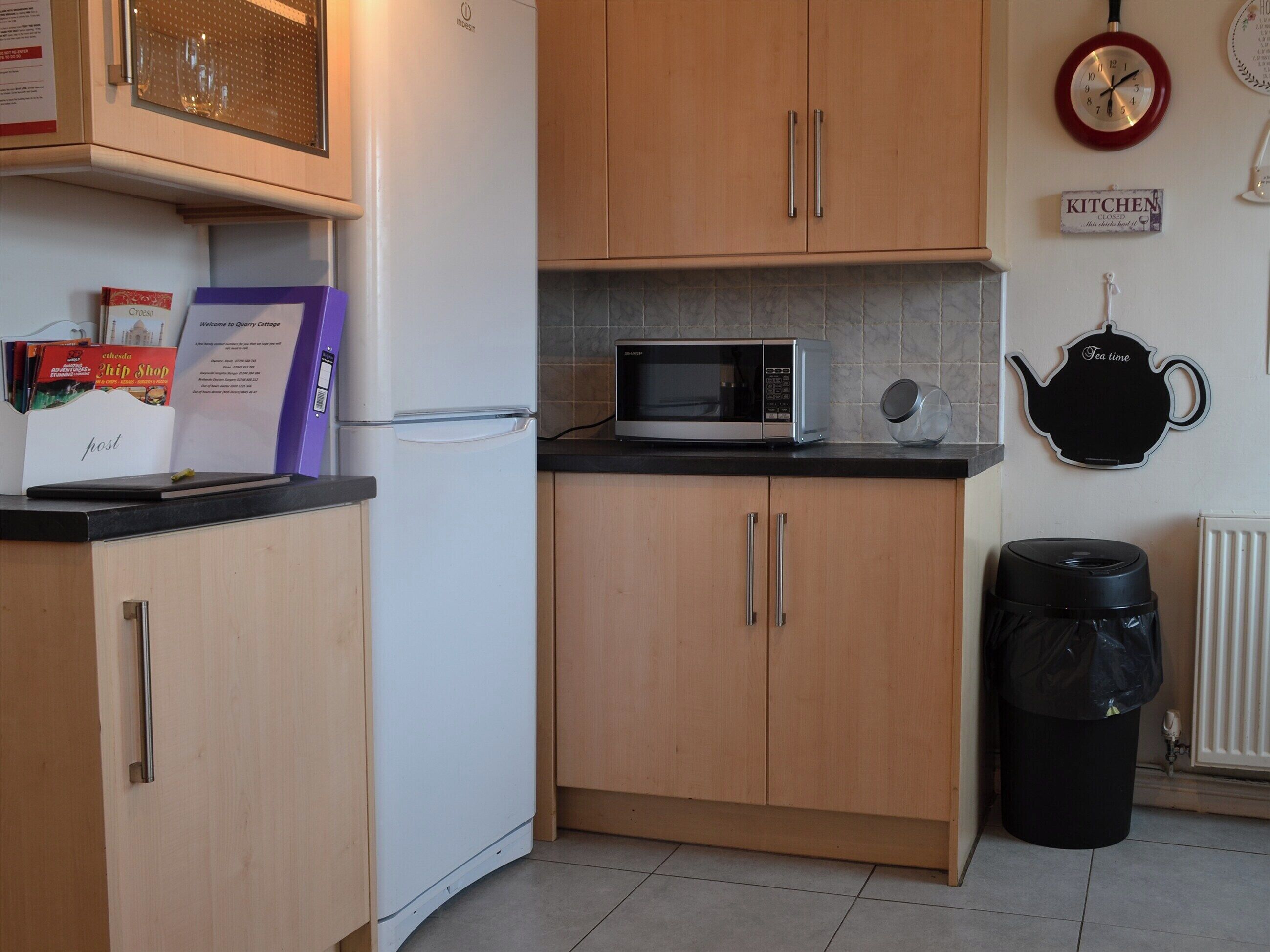 A compact kitchen with wooden cabinets, a white refrigerator, a microwave, and a kettle on the counter.