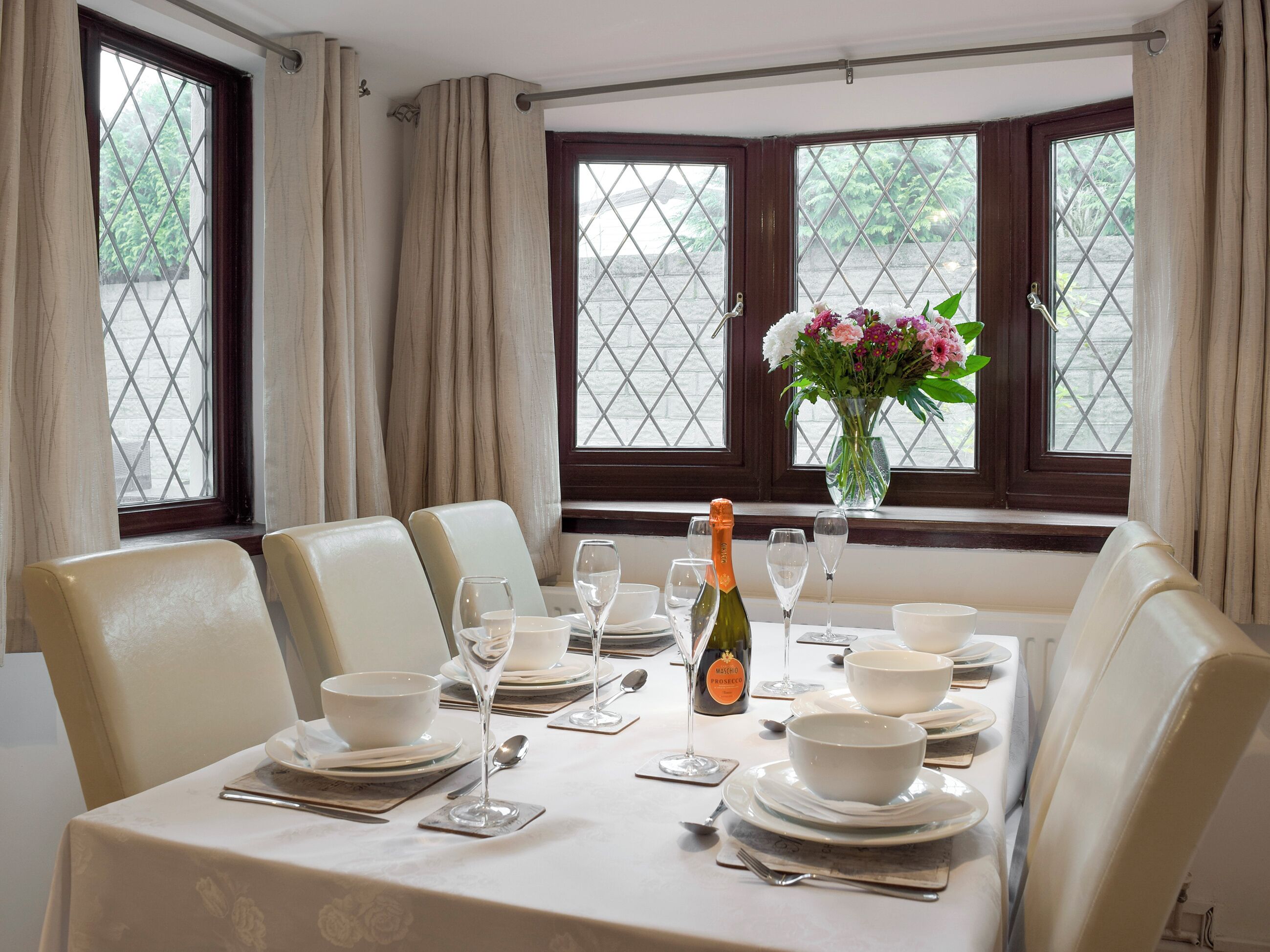 Une salle à manger avec une table dressée pour six personnes, comprenant des verres à vin, des assiettes et une bouteille de champagne.