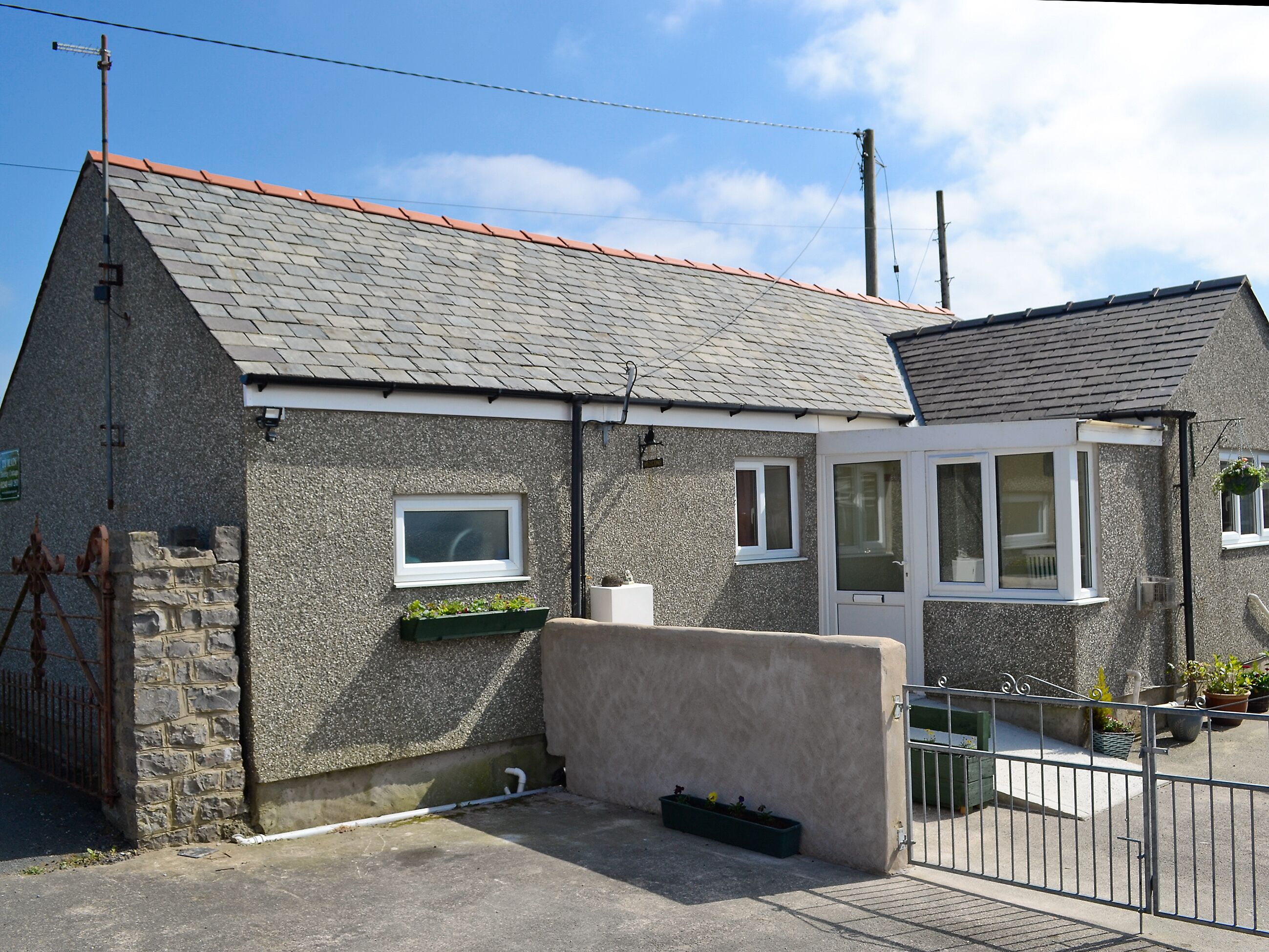 A two-story house with a stone exterior, a red-tiled roof, and a gated entrance.