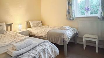 A bedroom with two beds, a nightstand, a bedside lamp, a window with curtains, and a radiator.