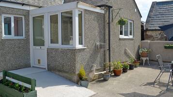 A house with a small porch, a window, and a door. There are potted plants and a bench.