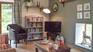 A living room with a leather armchair, a bookshelf, a television, and a window with a decorative horse figure. - 3 bedroom accommodation in Llanybri, near Carmarthen (Llanybri, near Carmarthen)
