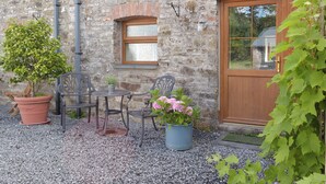 A stone building with a wooden door, a window, and a small table with chairs. There are potted plants and a gravel ground. - 3 bedroom accommodation in Llanybri, near Carmarthen (Llanybri, near Carmarthen)