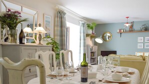 A dining area with a table set for four, surrounded by white chairs. There are two lamps, a mirror, and a shelf with decorative items. - 3 bedroom accommodation in Llanybri, near Carmarthen (Llanybri, near Carmarthen)