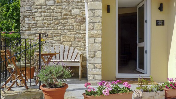 A stone building with a wooden chair and potted plants on the porch. - 2 bedroom accommodation in Spring Gardens, Frome (Spring Gardens, Frome)