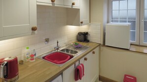 A kitchen with white cabinets, a stainless steel sink, a coffee maker, and a red kettle. - 2 bedroom accommodation in Spring Gardens, Frome (Spring Gardens, Frome)