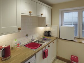 A kitchen with white cabinets, a stainless steel sink, a coffee maker, and a red kettle.