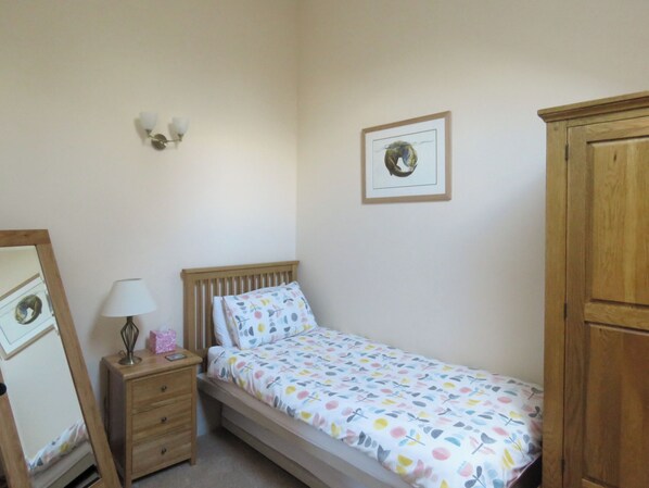 Een slaapkamer met een enkel bed, een nachtkastje met een lamp, een dressoir, een spiegel en een lijst met een afbeelding aan de muur.