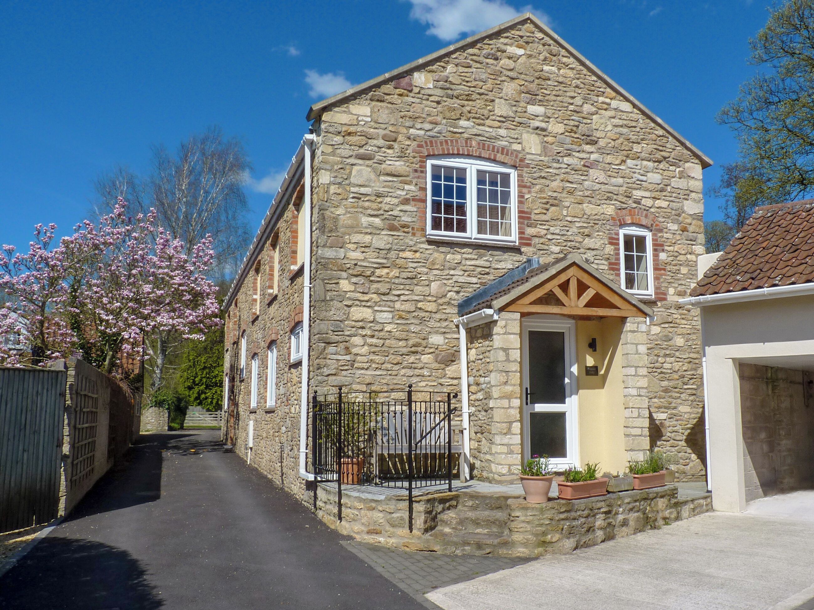 A stone building with a gabled roof, a small porch with potted plants, and a narrow street.