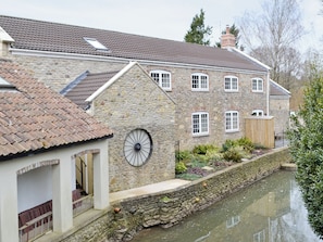 A stone building with a tiled roof, a water channel, and a wooden fence.