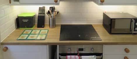 Una cocina con gabinetes blancos, un microondas, una estufa y varios utensilios de cocina.
