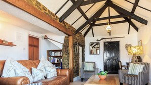 A cozy living room with a leather sofa, striped armchairs, a wooden coffee table, and a bookshelf. - 7 bedroom accommodation in West Pentire (West Pentire)