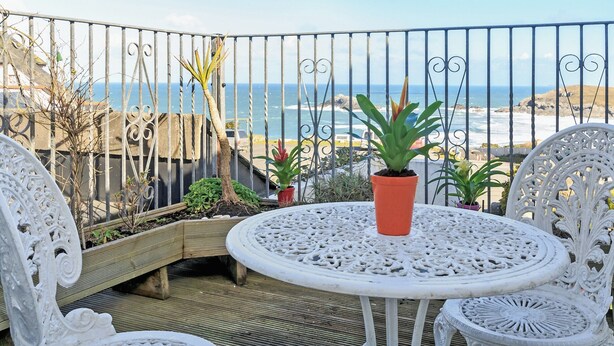 A balcony with a view of the ocean, featuring a round table and white chairs. - 7 bedroom accommodation in West Pentire (West Pentire)
