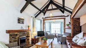 A cozy living room with a stone fireplace, wooden beams, striped furniture, and a television. - 7 bedroom accommodation in West Pentire (West Pentire)