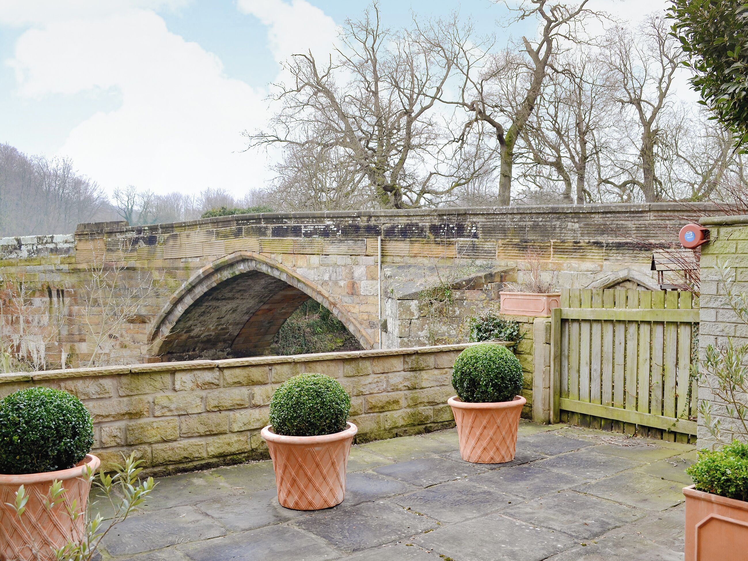 Un pont en pierre avec une arche, entouré d’arbres et de plantes en pot.