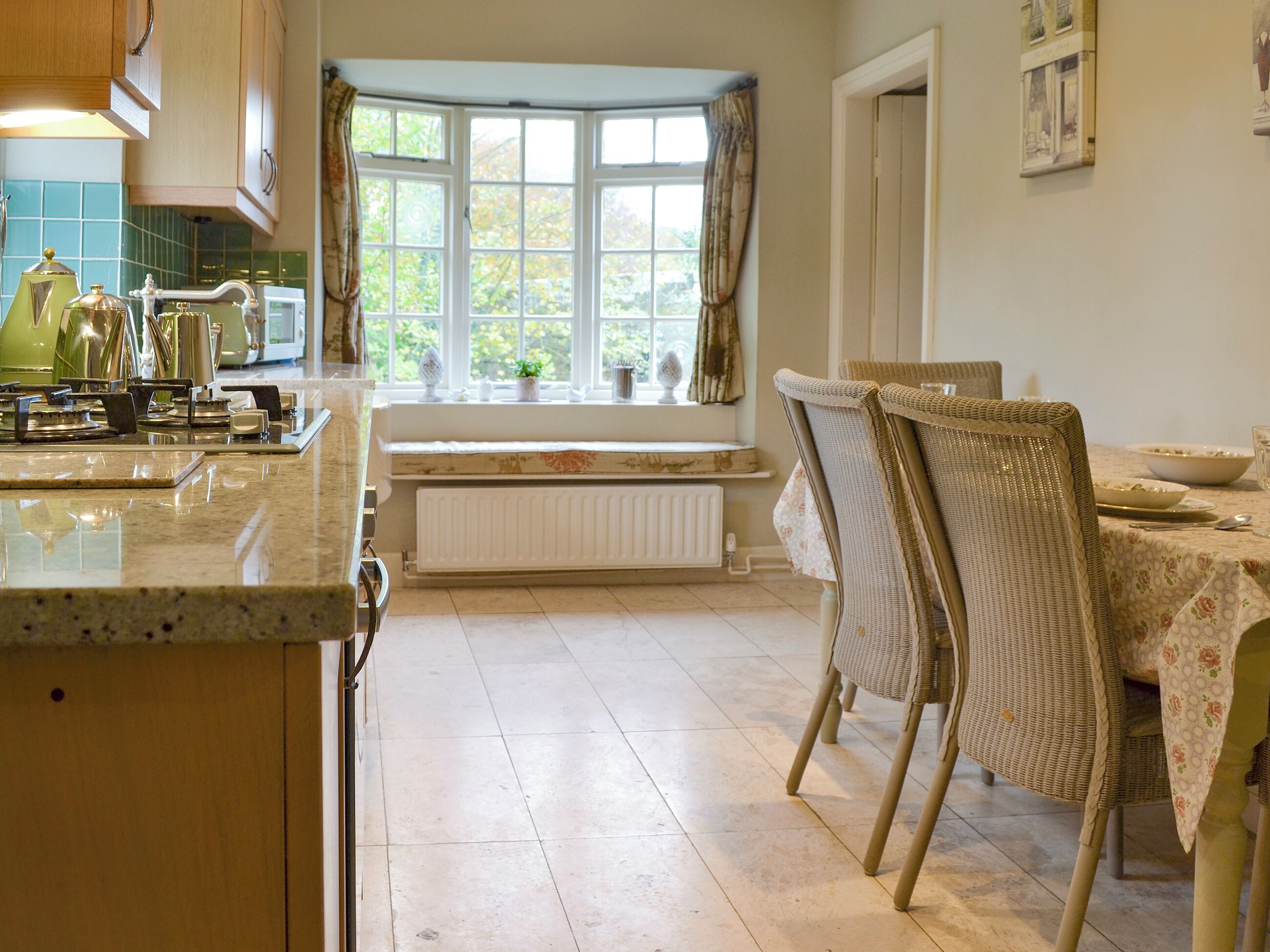 A kitchen with a bay window, a dining table with chairs, and a radiator.