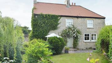 A stone house with a red-tiled roof, a garden with various plants and a small white umbrella.