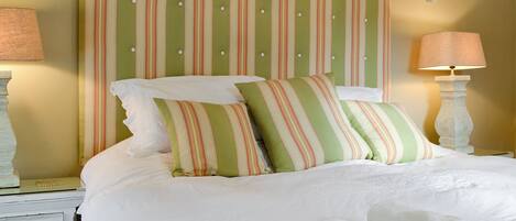 A neatly made bed with striped pillows and a headboard, a bedside table with a lamp, and a dresser with drawers.