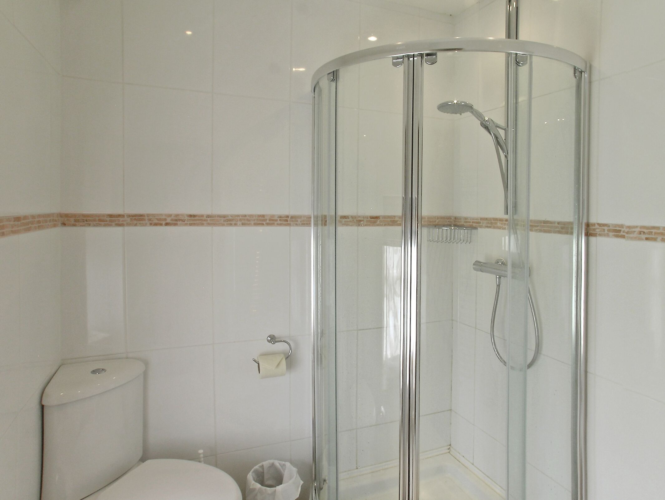Une salle de bain moderne avec une douche à parois de verre, des carreaux blancs et une bordure de couleur beige qui apporte une touche d’originalité.