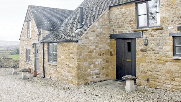 A stone building with a dark door, windows, and a chimney. - Dusty's Stable - E4751 (Ebrington, near Chipping Campden)