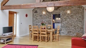 Un comedor con una mesa y sillas de madera, un televisor sobre un soporte, una pared de piedra y un sofá rojo.