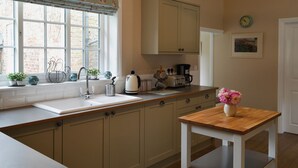 A kitchen with a window, a sink, cabinets, a coffee maker, and a vase with flowers on a table.