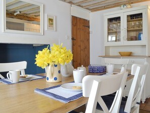 A dining area with a wooden table, white chairs, a vase of yellow flowers, and a kitchen with cabinets and a sink. - 2 bedroom accommodation in Near Holt (Near Holt)