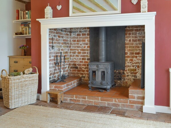 A cozy room with a brick fireplace, a small wooden stool, and a wicker basket. - 2 bedroom accommodation in Near Holt (Near Holt)