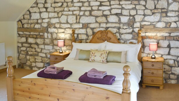 Un dormitorio con pared de piedra, cabecero de madera y dos mesitas de noche con lámparas.