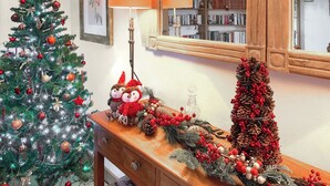 Un sapin de Noël, une lampe, un miroir et une composition décorative de pommes de pin sur une table en bois.