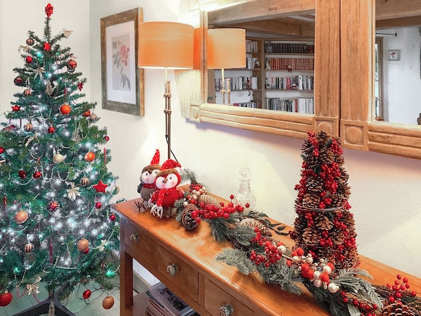 A Christmas tree, a lamp, a mirror, and a decorative pine cone arrangement on a wooden table.