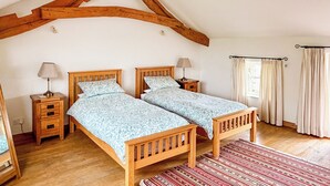 Une chambre à coucher avec deux lits en bois, un tapis rouge à motifs, des tables de chevet en bois et une fenêtre avec des rideaux.