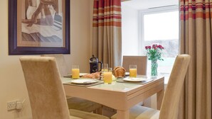 Un comedor con una mesa dispuesta para dos personas, una cafetera, croissants y jugo de naranja.