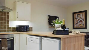 Una cocina moderna con microondas, lavavajillas y una pequeña zona de bar con una botella de champán y una bolsa de aperitivos.