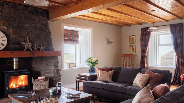 Ein gemütliches Wohnzimmer mit Kamin, einer Couch, einem Couchtisch mit Schachspiel und einer Steinwand.