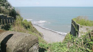 A coastal path leading to a beach with a stone wall and vegetation.