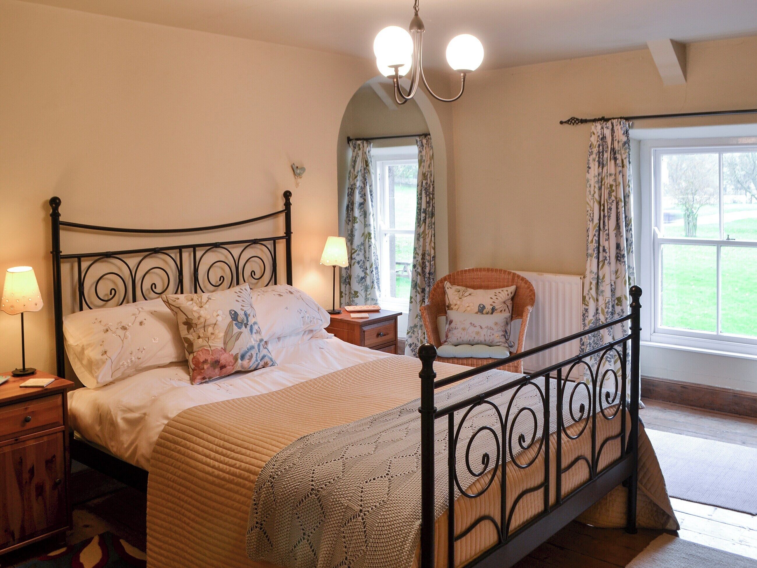 A bedroom with a bed, two bedside tables, a lamp, a chair, and a window with curtains.