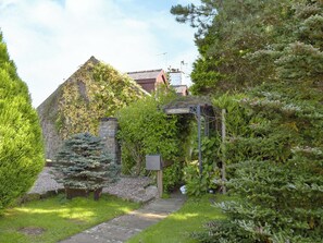 Een stenen gebouw met klimop, een houten pergola en een bord waarop 'SARDIS Cottages' staat.