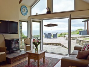 A living room with a fireplace, television, and a view of the sea through large glass doors. - 3 bedroom accommodation in Llangennith, near Swansea (Llangennith, near Swansea)