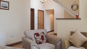A living room with a sofa, a chair, a wooden floor, a chandelier, and a door. - 3 bedroom accommodation in Llangennith, near Swansea (Llangennith, near Swansea)
