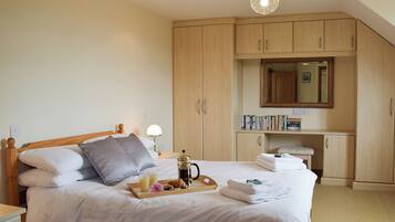 A neatly made bed with a tray of breakfast items, a bedside table with a lamp, and a large mirror above a wooden cabinet.
